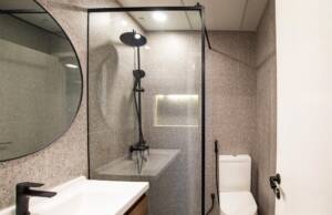 Modern minimalist bathroom with gray textured tiles, black fixtures, glass shower enclosure, and sleek white toilet, creating a contemporary and elegant space.