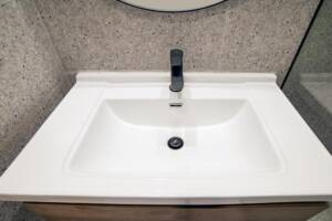 Sleek white bathroom sink with modern black faucet on gray tiled wall background.