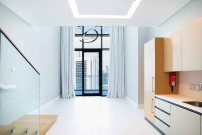 Modern high-rise apartment with sleek minimalist kitchen, large floor-to-ceiling windows, and cityscape view, featuring contemporary lighting and elegant white and wood accents.