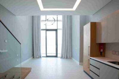 Modern minimalist living space with large glass door and white curtains, bright natural light, contemporary ceiling design, and integrated kitchen area featuring sleek cabinetry and utility sink.