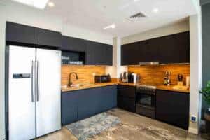 Modern black kitchen with wooden countertops, stainless steel appliances, and open shelving for glassware and spices. Features a refrigerator, microwave, coffee maker, and a stylish backsplash. Perfect for contemporary home cooking.
