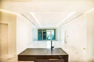 Spacious modern living room with bright natural light, minimalist decor, and sleek architectural design, featuring a central island and large glass doors leading to a balcony.