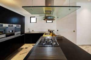 Modern kitchen with black cabinetry and stainless steel appliances, featuring a gas cooktop and innovative glass ceiling design for a sleek, contemporary look.
