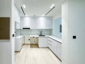 Modern minimalist white kitchen with sleek cabinetry, marble backsplash, and black accents, designed for contemporary living spaces in Dubai.