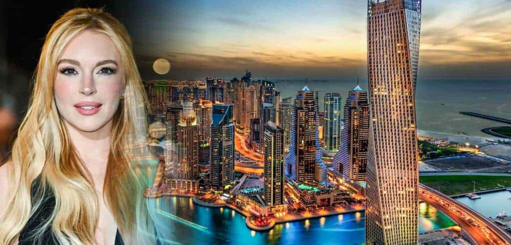 Modern city skyline at dusk with illuminated skyscrapers, featuring a prominent twisting tower along a waterfront with vibrant lights and a sunset sky.