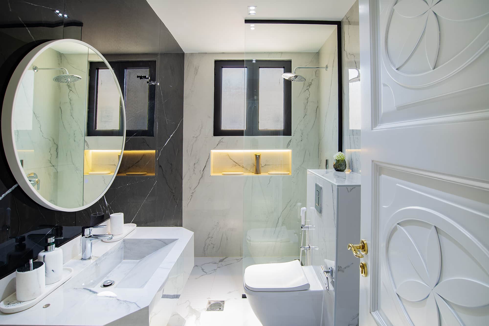 Sleek modern bathroom with marble walls, large oval mirror, black window frames, glass shower enclosure, and minimalist fixtures, creating a luxurious and stylish space.