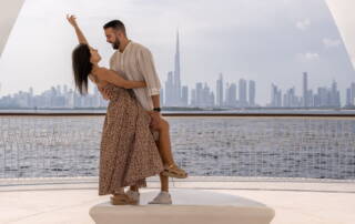 Romantic couple dancing on balcony with Dubai skyline in background, Burj Khalifa visible, water view, outdoor, cityscape, lifestyle, travel, love, vacation, modern architecture, skyline.