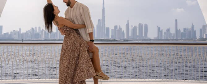 Romantic couple dancing on balcony with Dubai skyline in background, Burj Khalifa visible, water view, outdoor, cityscape, lifestyle, travel, love, vacation, modern architecture, skyline.