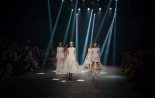 Dazzling fashion runway show with models in elegant white gowns under spotlight in Dubai.