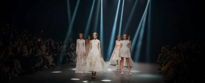 Dazzling fashion runway show with models in elegant white gowns under spotlight in Dubai.